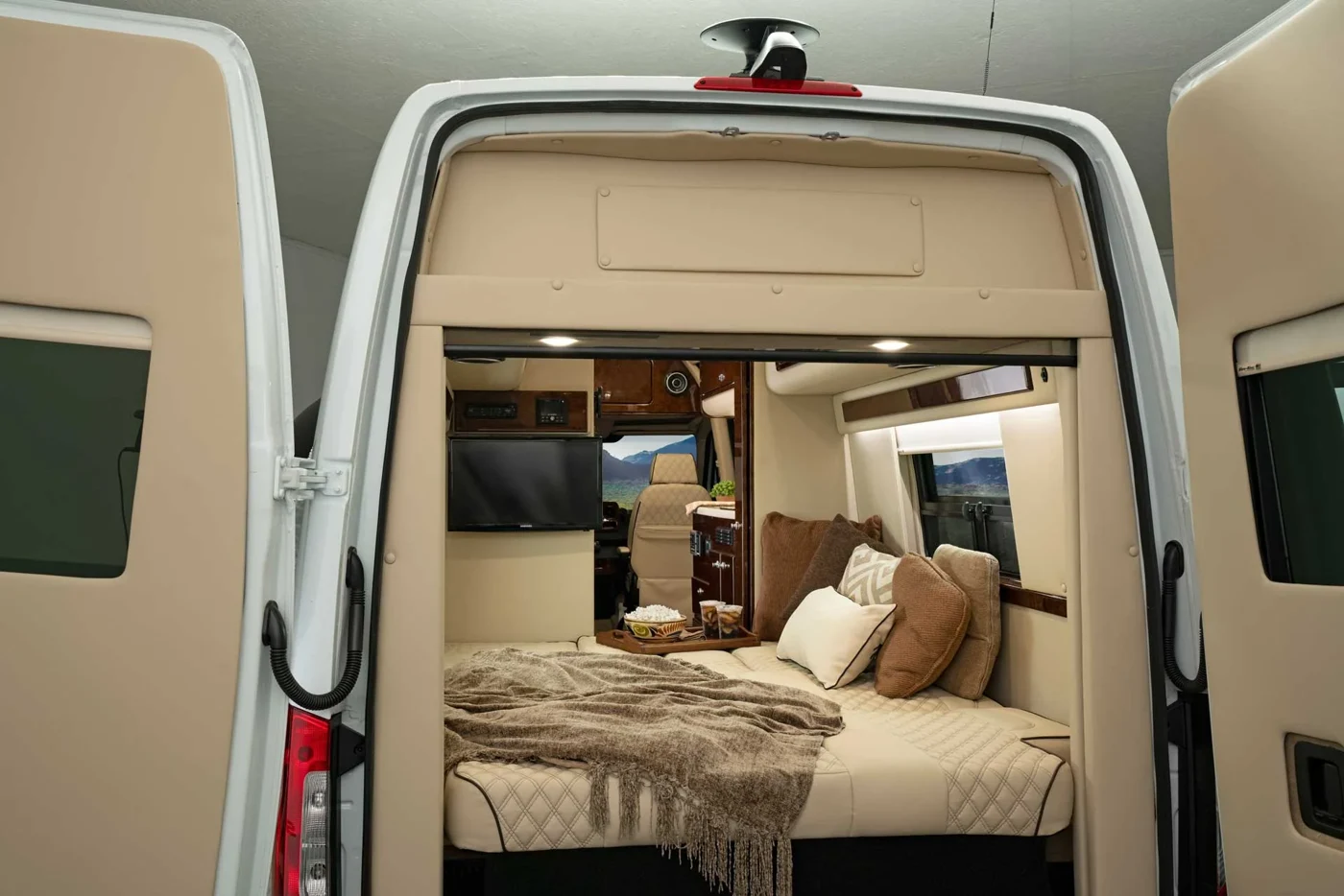 Open rear doors of a Sprinter camper conversion showing the bed and galley